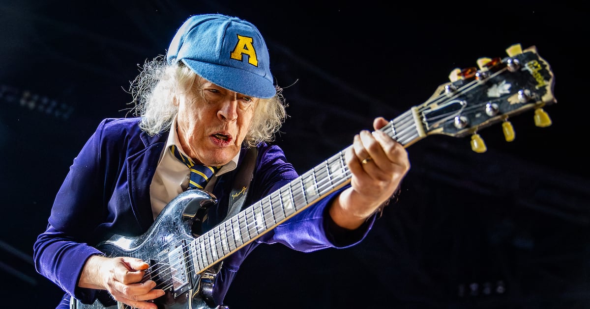 Angus Young of AC/DC performing under the band's neon logo at Mercedes-Benz Stadium
