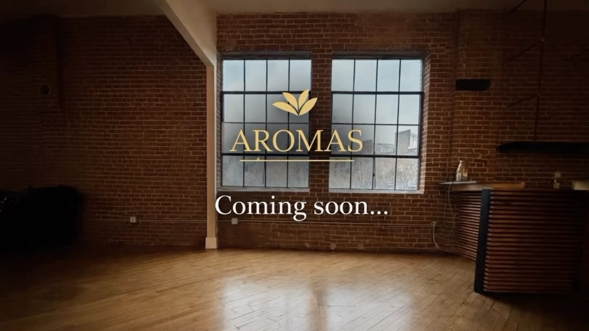 Empty brick-walled loft space at 141 Mangum St. SW with tall factory windows and a wood bar, overlaid with the Aromas logo and "Coming soon"