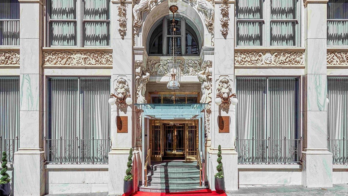 Marble facade and arched Peachtree Street entrance of The Candler Hotel in downtown Atlanta, with carved lions and a red carpet at the steps