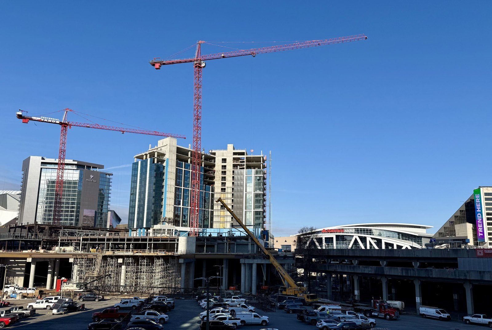 Tower cranes rise over Centennial Yards construction in Downtown Atlanta, with State Farm Arena on the right under a clear blue sky