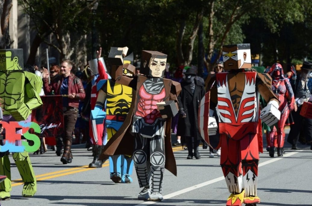 Dragon Con parade marchers in boxy cardboard superhero costumes walking down a downtown Atlanta street