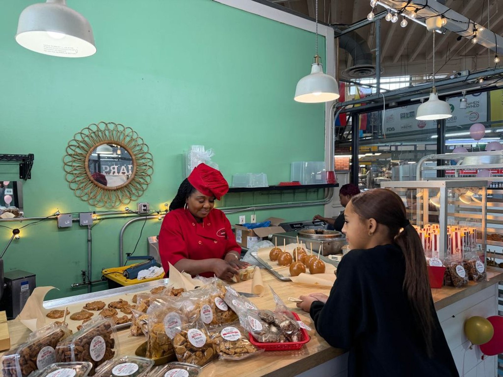 A vendor in a red chef's coat serves a young customer at Miss D's candy counter inside the Municipal Market