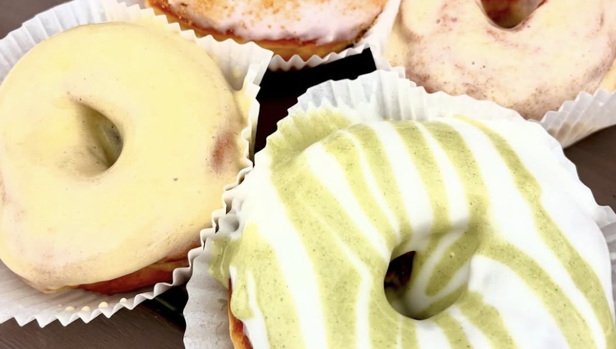 Close-up of glazed sour cream doughnuts in paper liners, one striped with green and white icing