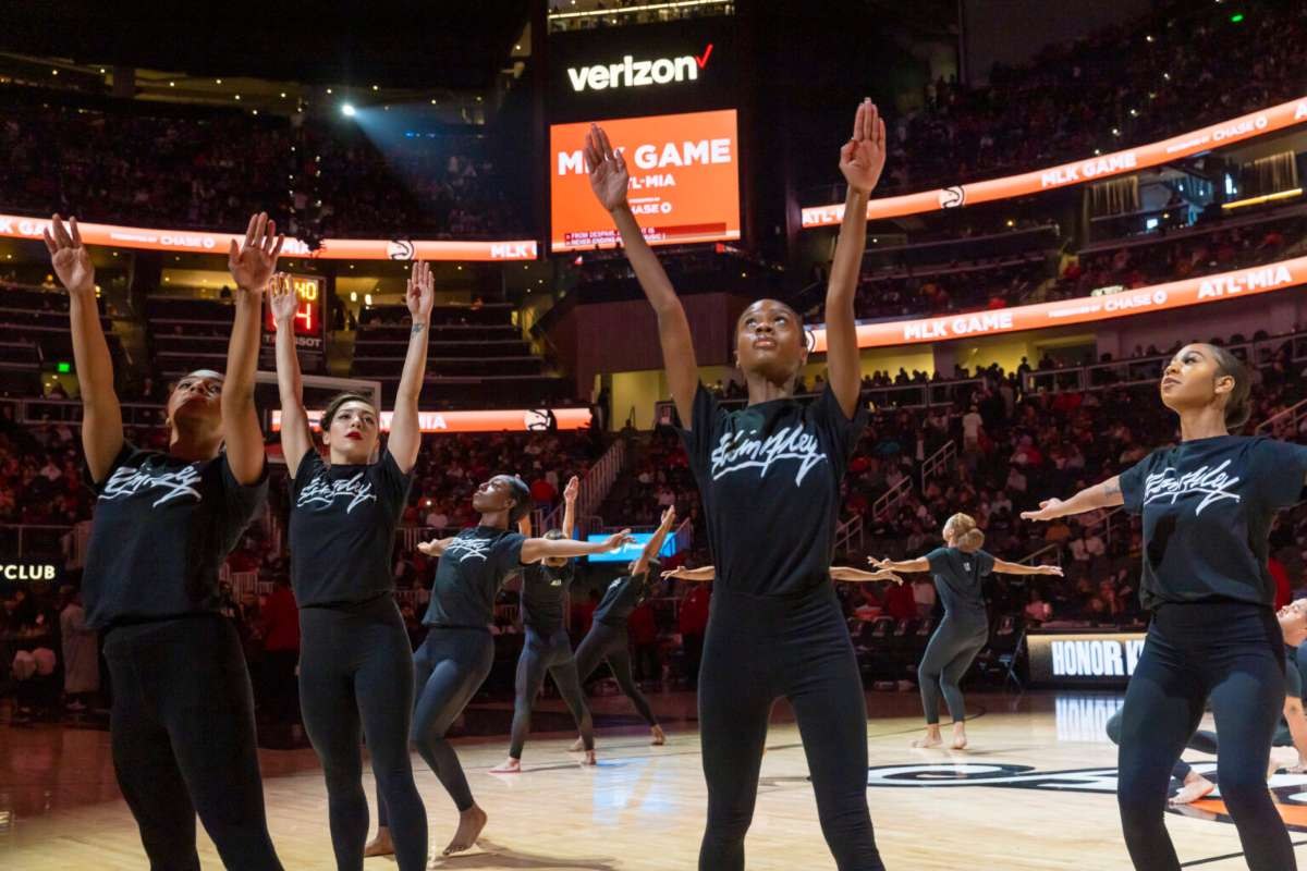 Dancers in black shirts raise their arms on the court at State Farm Arena during a Hawks MLK Day game