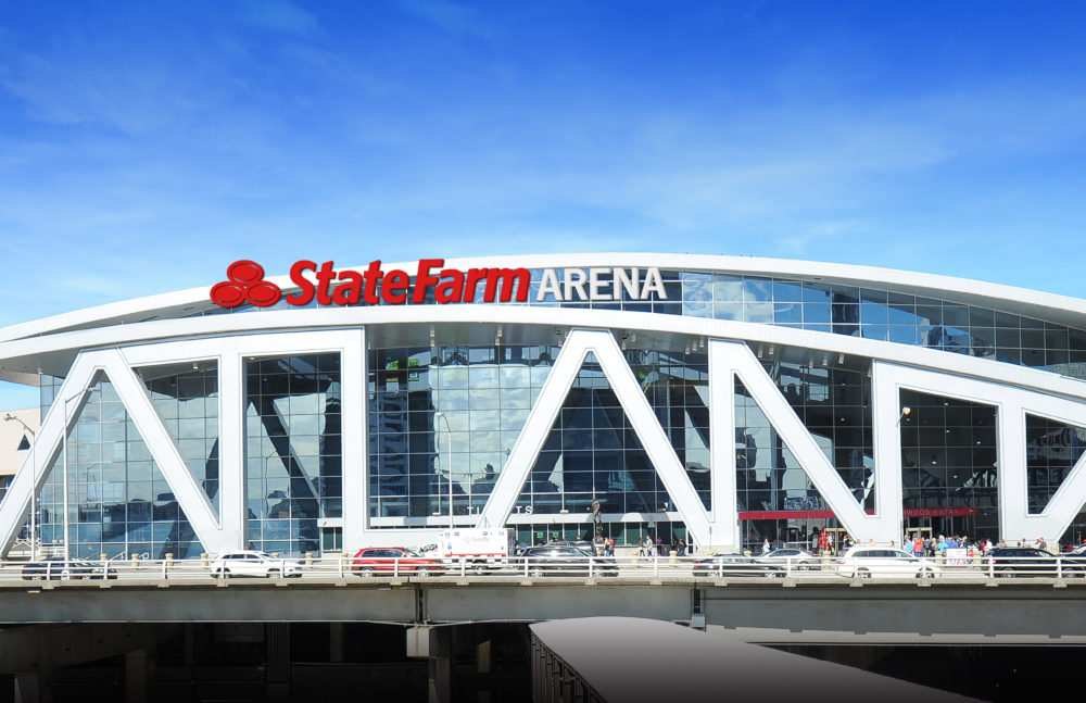 Exterior of State Farm Arena in downtown Atlanta, with its red and white sign above a glass facade and white angled supports under a blue sky