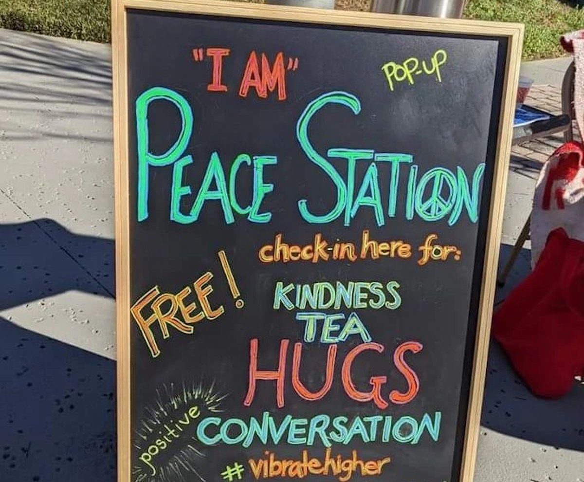 Hand-lettered chalkboard sign for the "I AM" Peace Station pop-up offering kindness, tea, hugs and conversation