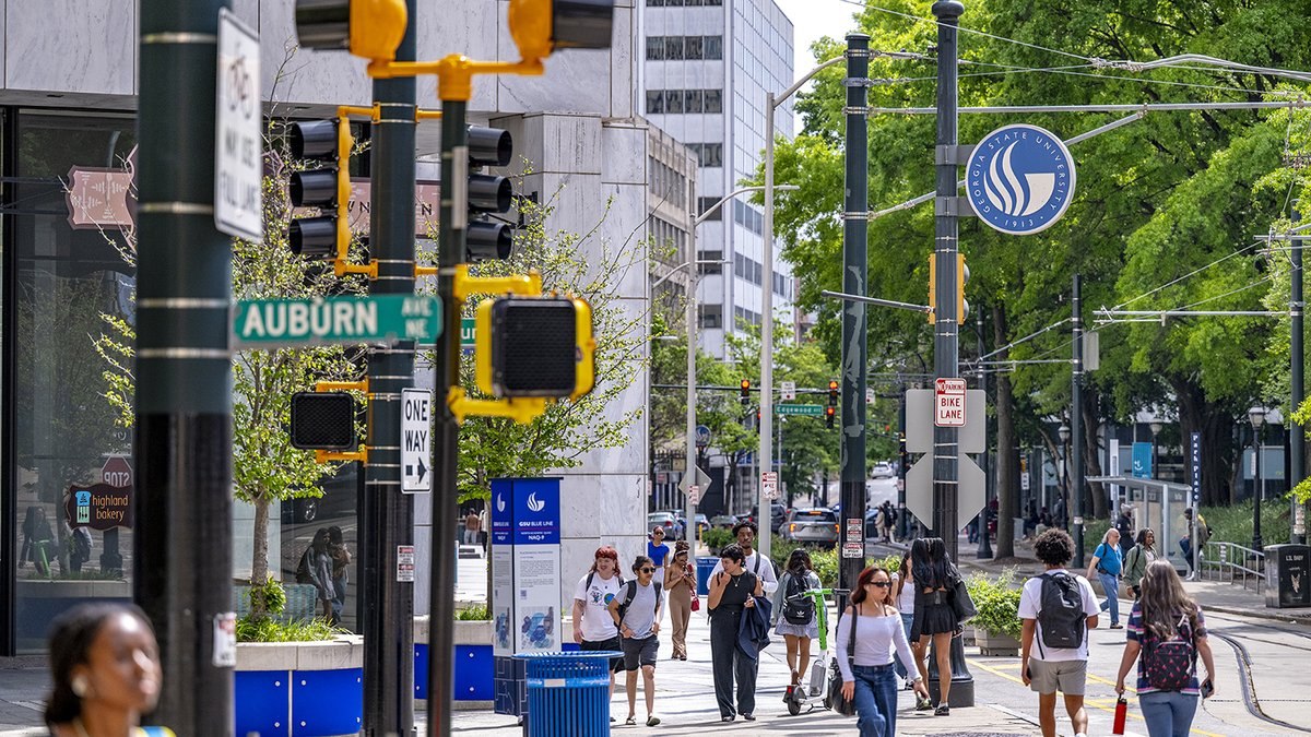 Students walking along Decatur Street past Georgia State University signage and the GSU Blue Line at Auburn Avenue in downtown Atlanta