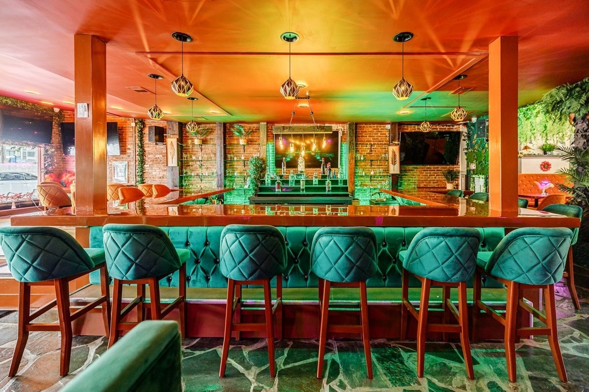 The bar at Miss Conduck on Edgewood Avenue, with teal velvet bar stools, exposed brick walls, hanging pendant lights and plants