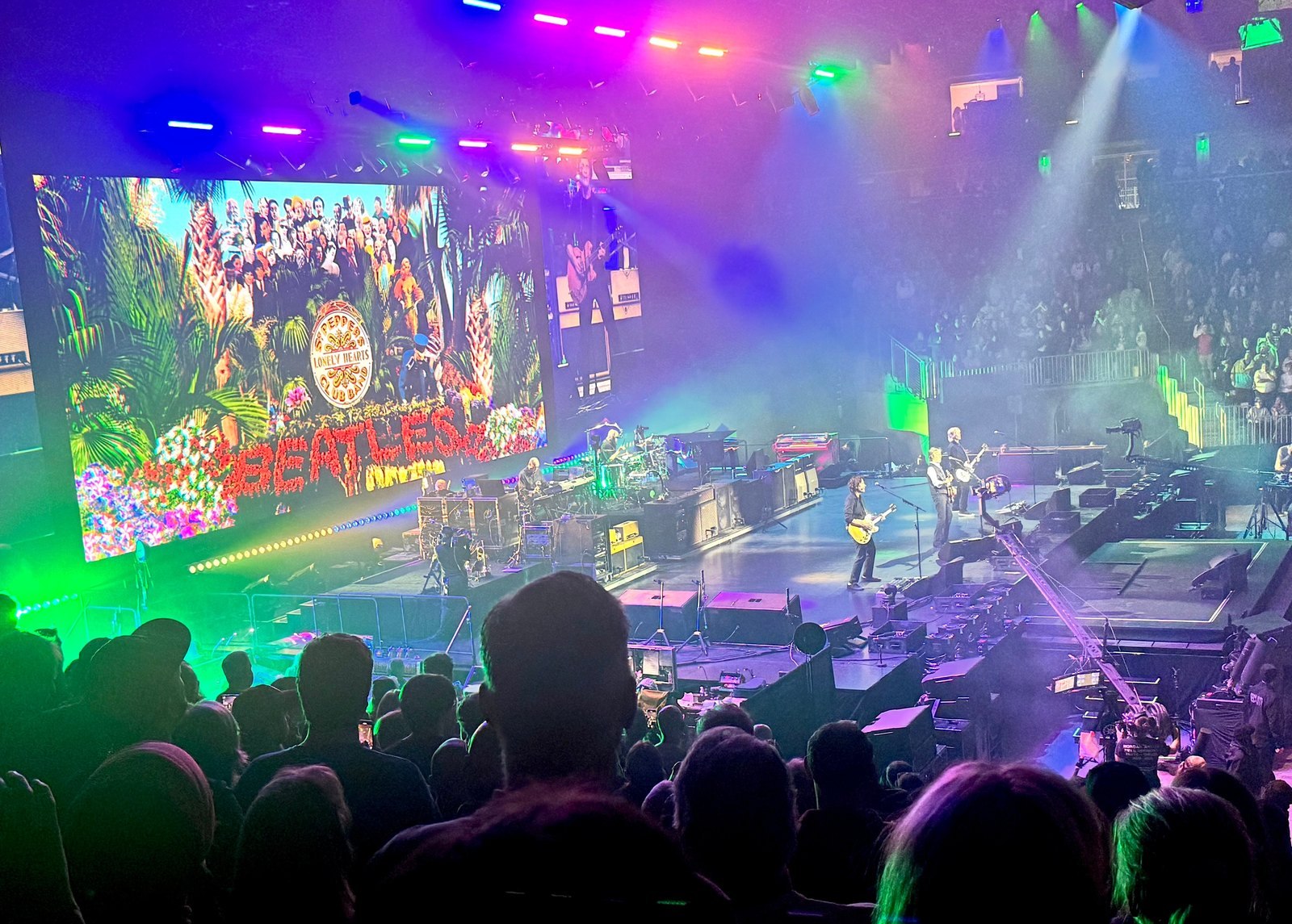 Paul McCartney and his band perform on stage at State Farm Arena beside a giant screen showing Sgt. Pepper's Lonely Hearts Club Band artwork