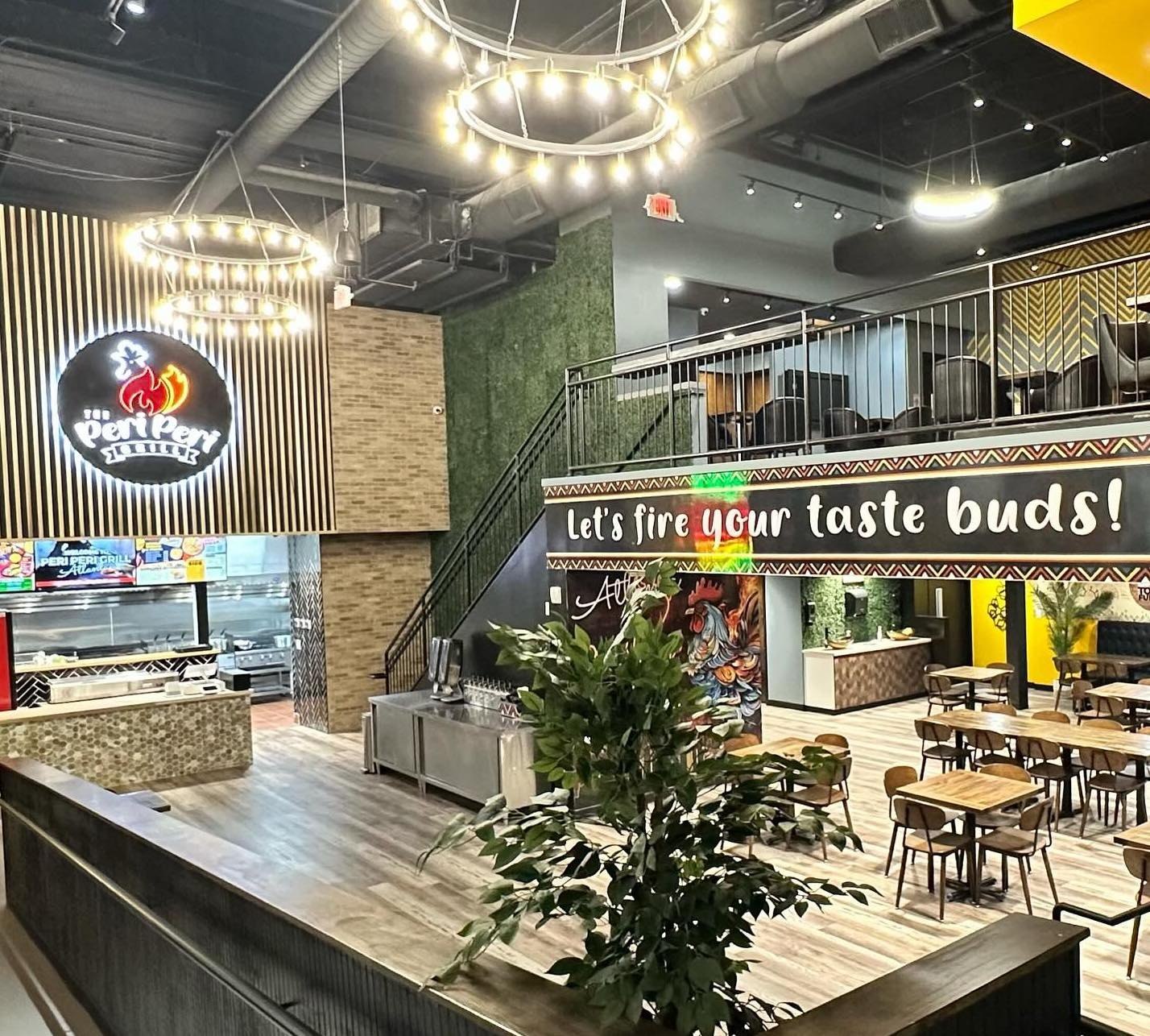 Interior of The Peri Peri Grill on Luckie Street, with the lit logo above the order counter, a dining room of wood tables and a second-floor mezzanine