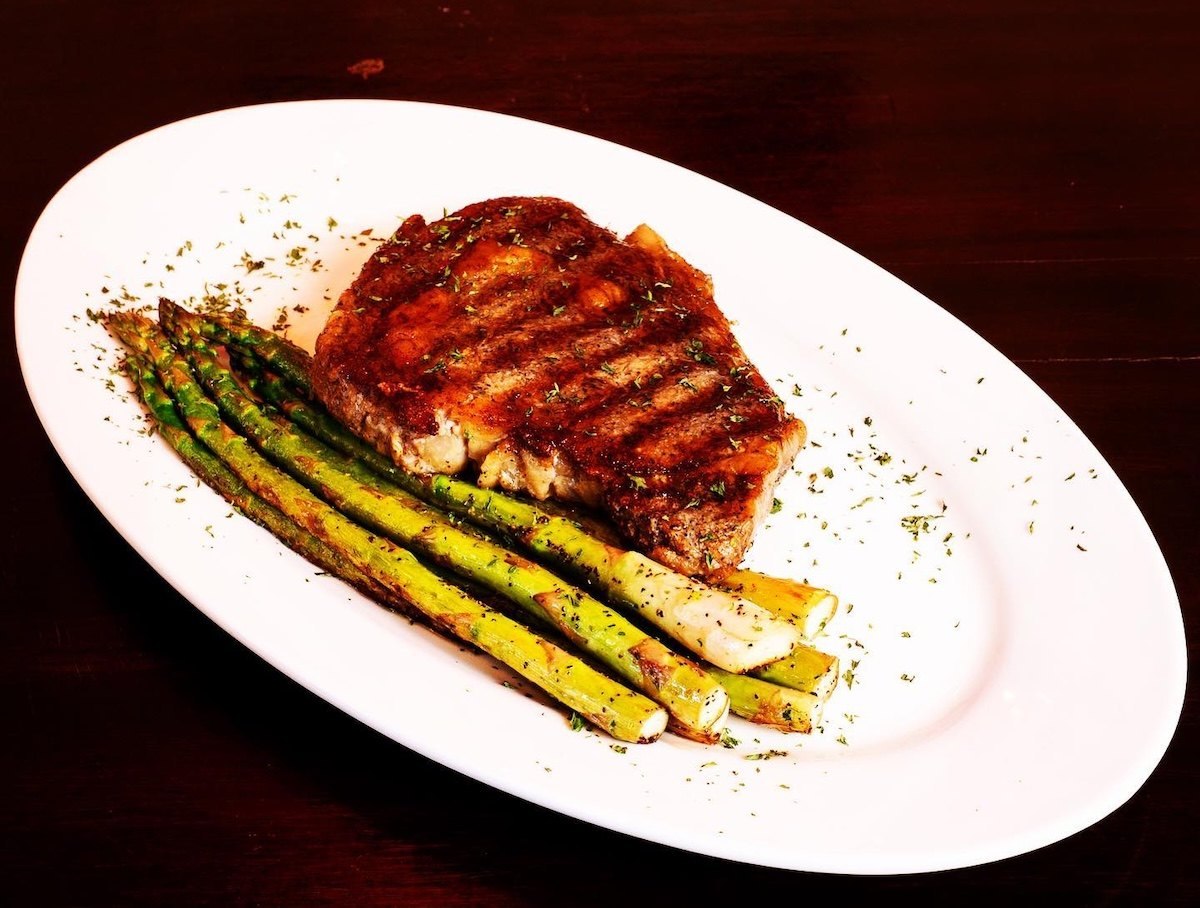 A grilled steak with roasted asparagus on a white oval platter