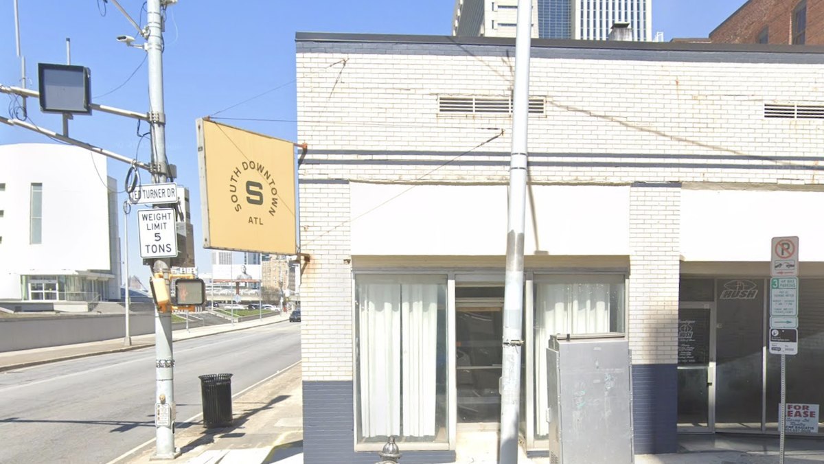White brick storefront on Mitchell Street with a gold South Downtown ATL sign at the corner of Ted Turner Drive