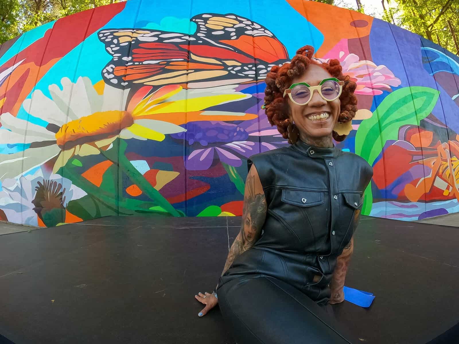 Artist Charity Hamidullah sitting in front of the Wild Seed, Wild Flower mural of butterflies and flowers (photo via ATL Direct)