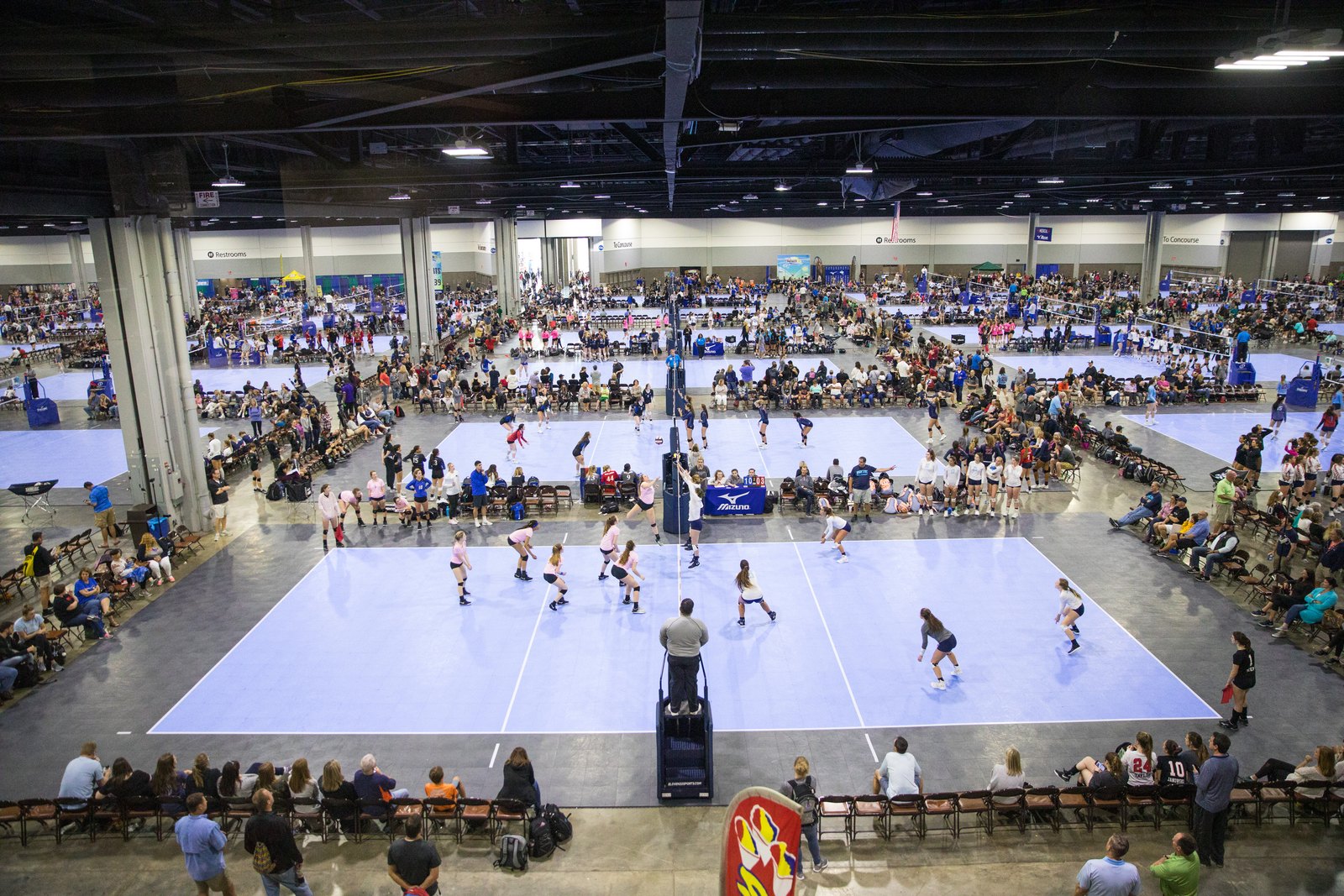 Overhead view of rows of pale blue volleyball courts in a Georgia World Congress Center exhibit hall during the Big South National Qualifier, with junior teams in play and spectators lining the sidelines