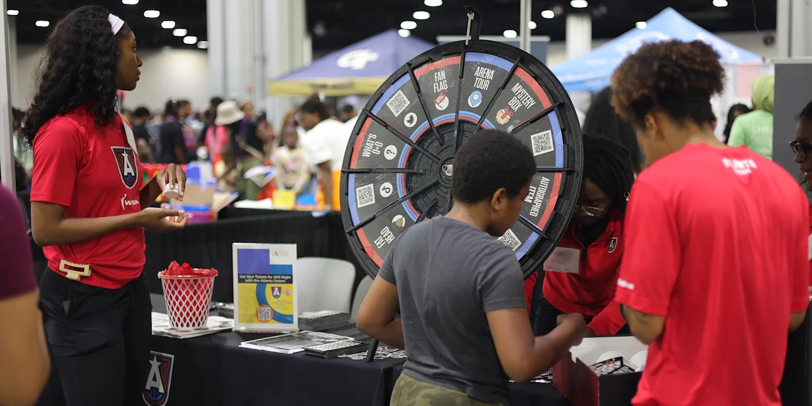 Students and families gather at an Atlanta Dream prize-wheel booth inside a Georgia World Congress Center exhibit hall during the Atlanta Public Schools Back to School Bash.