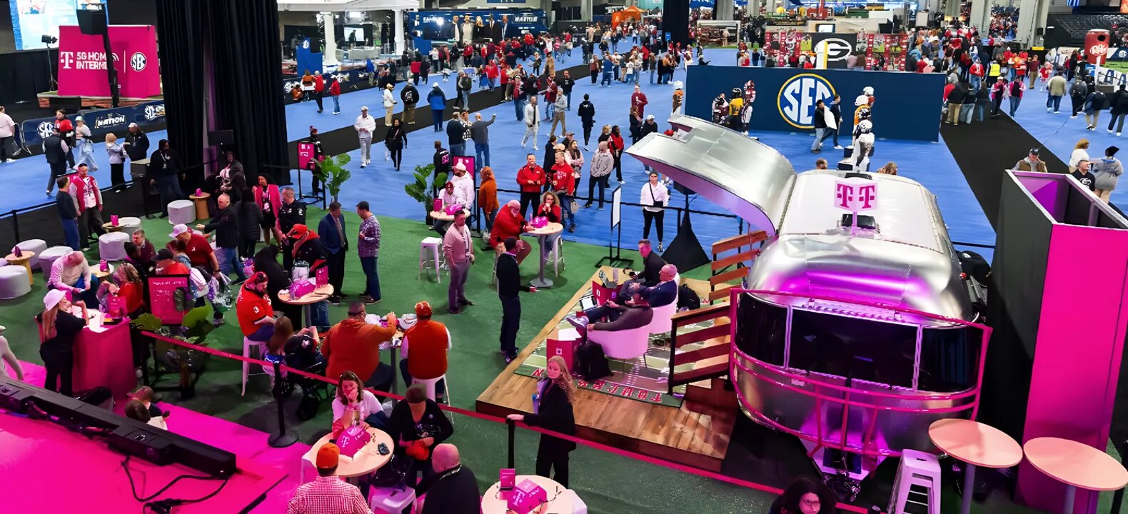 Elevated view of the Dr Pepper SEC FanFare floor at the Georgia World Congress Center, with fans in team colors moving among interactive booths beneath a large SEC logo backdrop