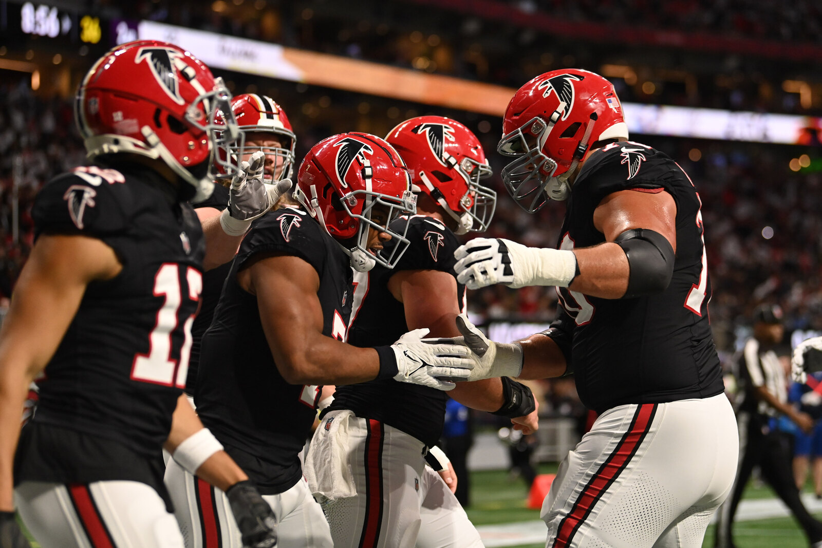 Atlanta Falcons players in black home jerseys and red helmets celebrate a touchdown in the end zone against the New Orleans Saints at Mercedes-Benz Stadium