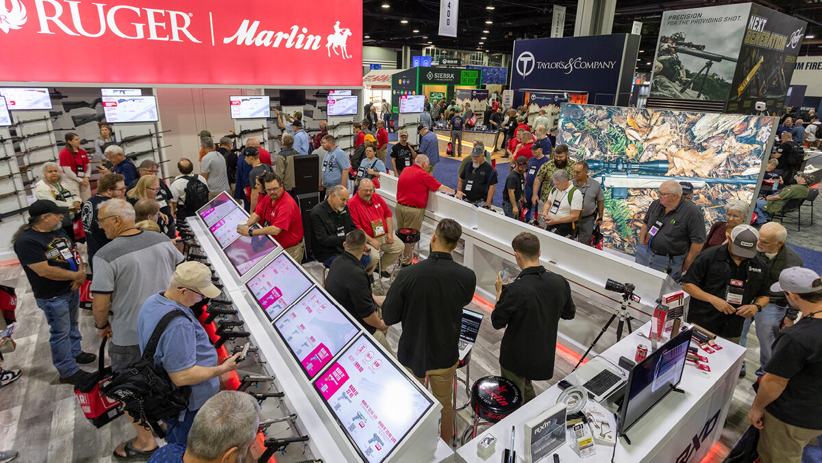 Attendees browse exhibitor booths on the crowded NRA Annual Meetings exhibit hall floor beneath a Ruger and Marlin banner at the Georgia World Congress Center