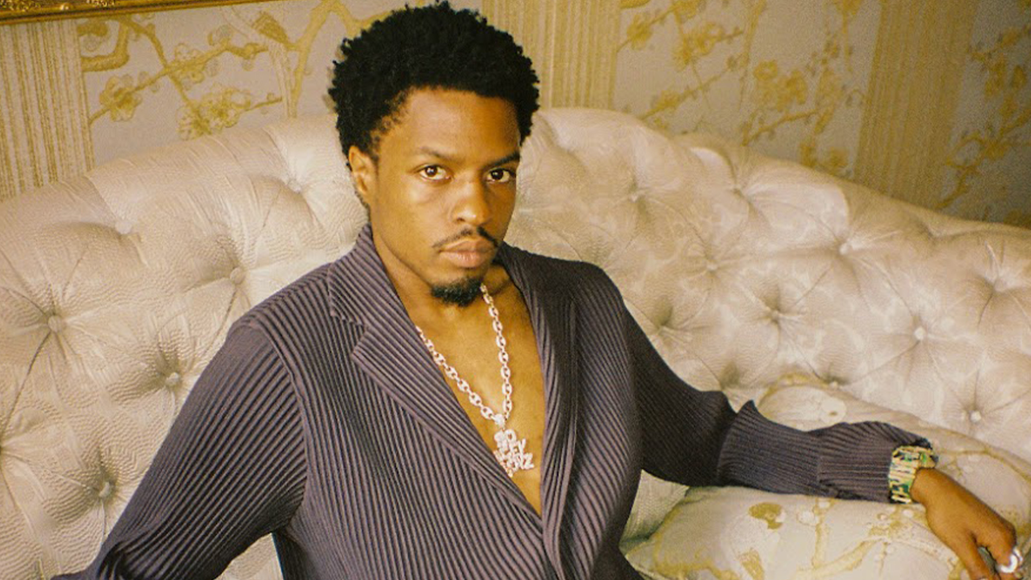 Rapper and producer Pi'erre Bourne seated on a tufted cream sofa in a pinstriped open jacket and diamond chain, promotional art for his Made In Paris show at Hell at The Masquerade.