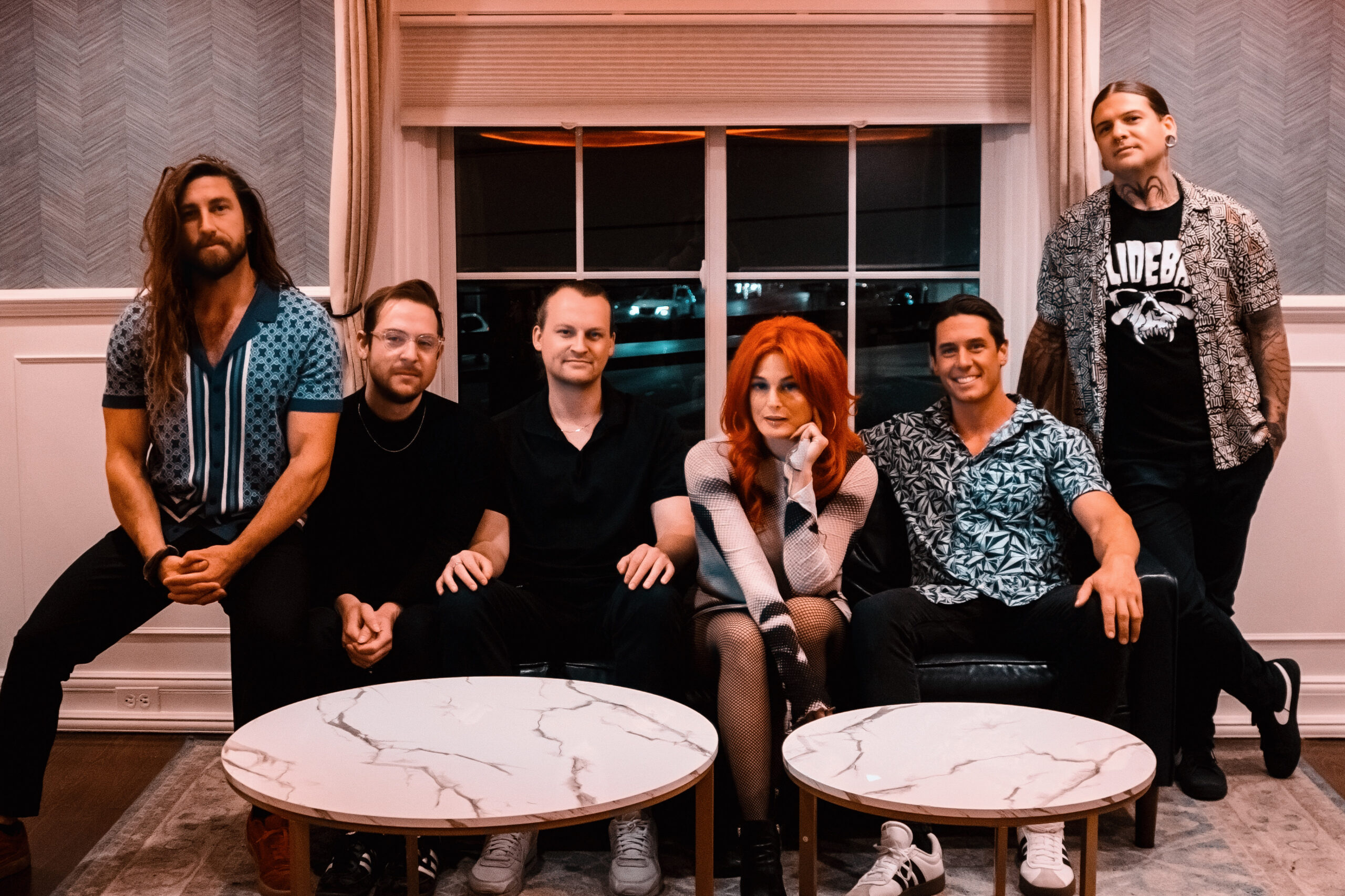 Save Ferris band members posed together in a warmly lit lounge, with frontwoman Monique Powell's bright red hair anchoring the center of the group.