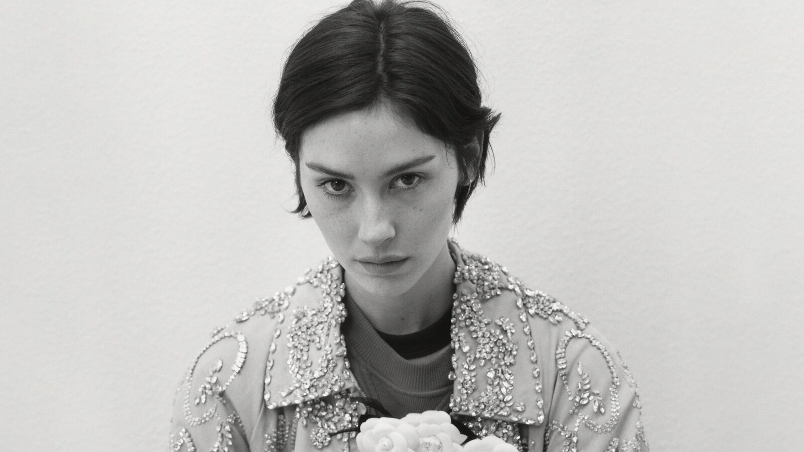 Black-and-white press portrait of singer Gracie Abrams looking directly at the camera in a crystal-embellished jacket