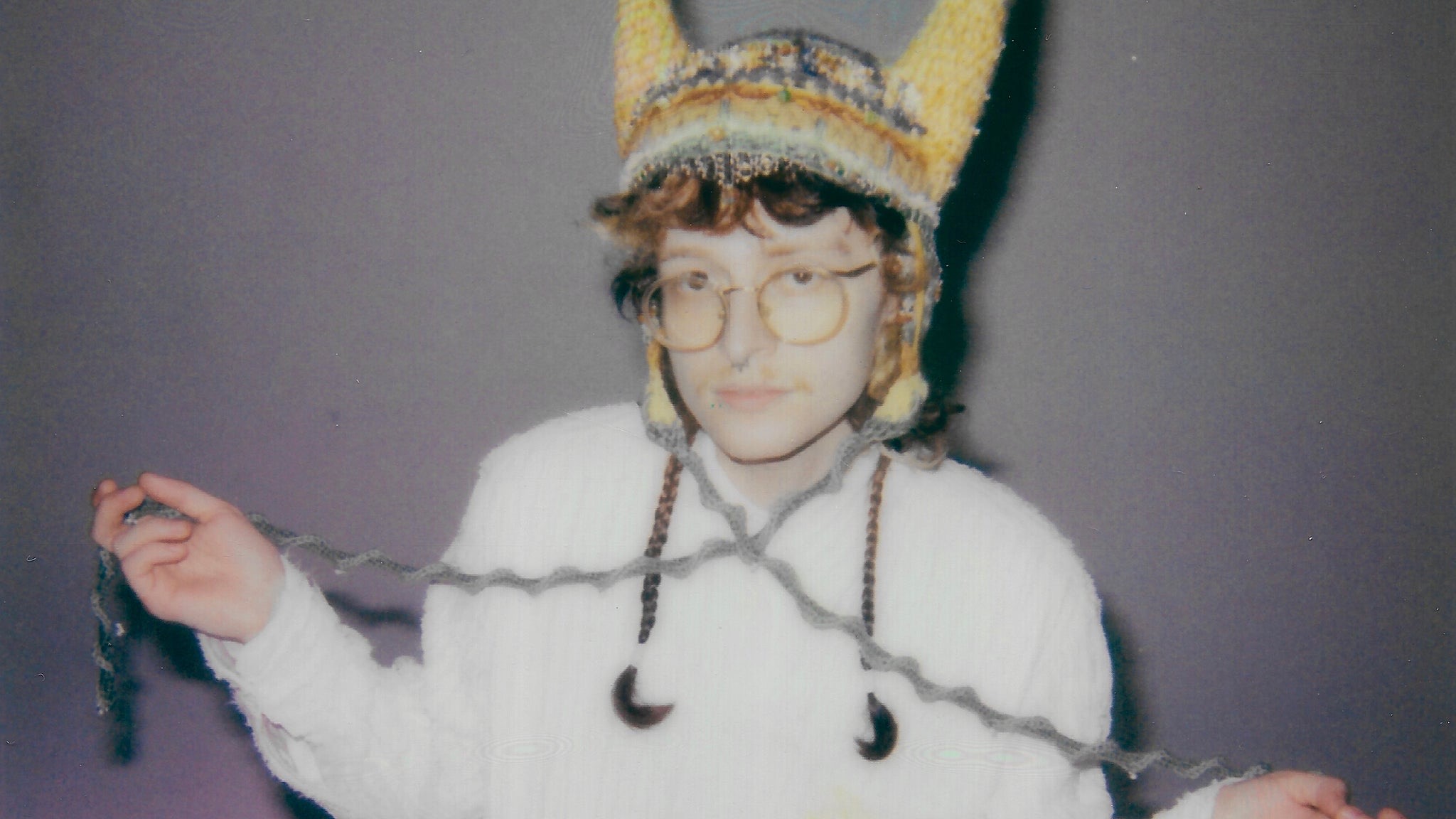 Cavetown (Robin Skinner) in a yellow knit horned hat and white cable-knit sweater, official promo art for the Running With Scissors Tour with Chloe Moriondo.