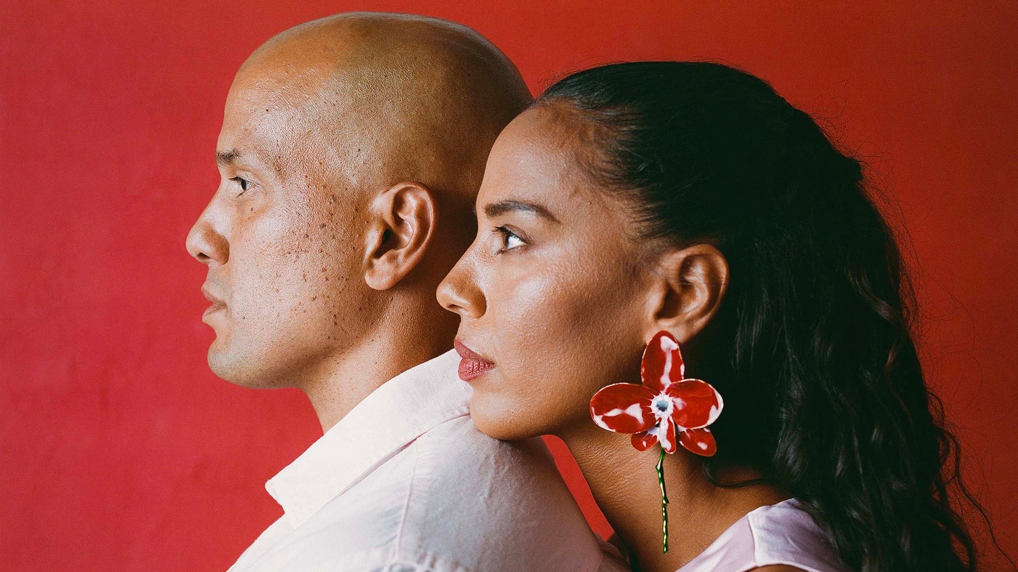 JOHNNYSWIM duo Abner Ramirez and Amanda Sudano Ramirez standing back-to-back in profile against a deep red wall, promo art for the Greetings from Georgica Pond 10-Year Anniversary Tour.