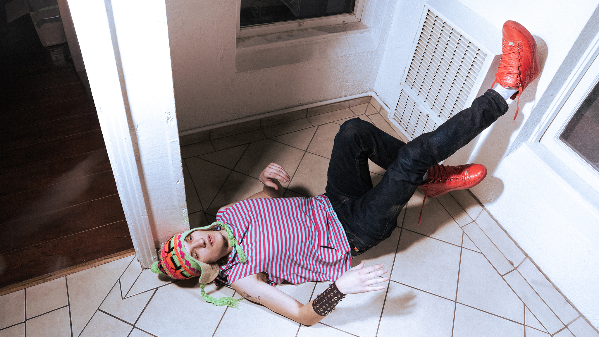 Musician Tommy Fleece lying on a tiled floor in a striped shirt and red boots